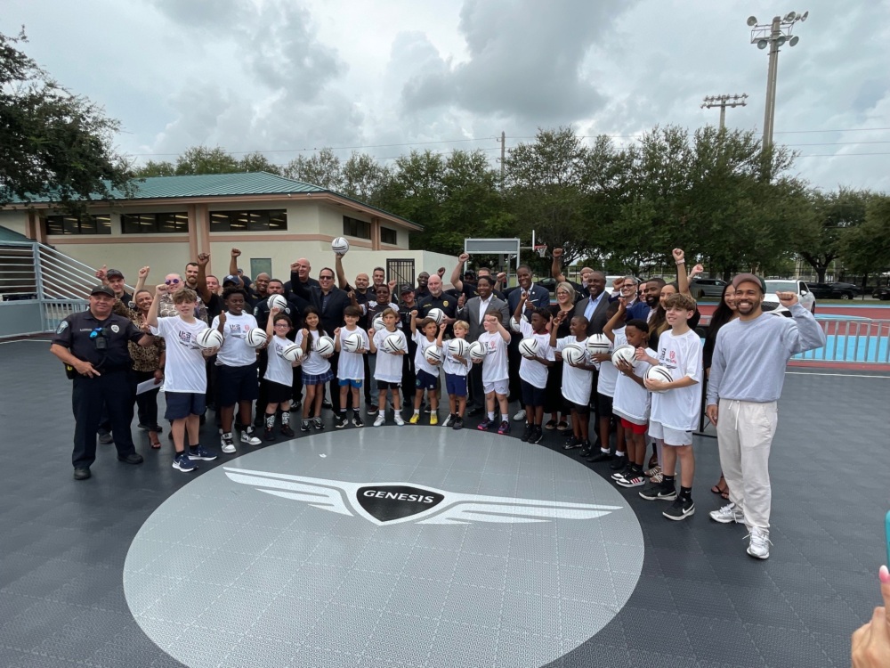 about 45 adult and children smile at the camera with hands in the air. the kids are wearing white shirts. a few adults in the crowd wear their Hollywood PD uniform.